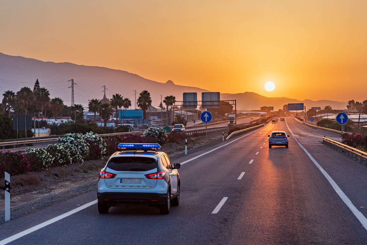 Un coche de la policía de tráfico circulando por una autopista con el sol de la madrugada asomando por las montañas.